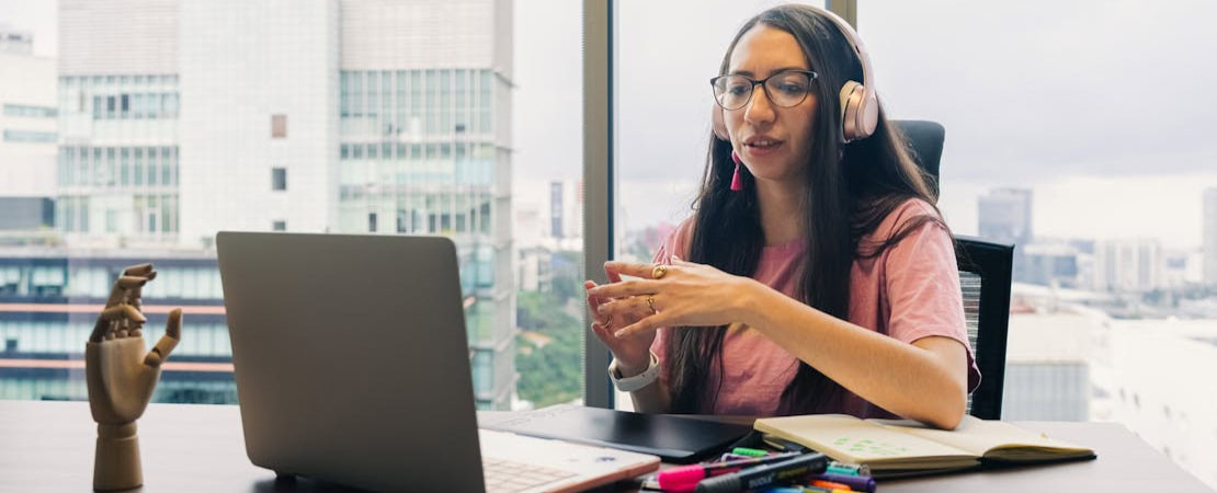 Imagem mostrando uma mulher fazendo uma aula de inglês ao vivo com um laptop em seus escritório.
