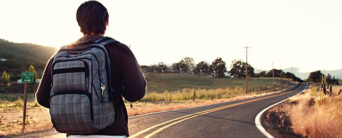 Imagem mostrando um homem com uma mochila em uma estrada, representando as aulas de inglês com falantes nativos.