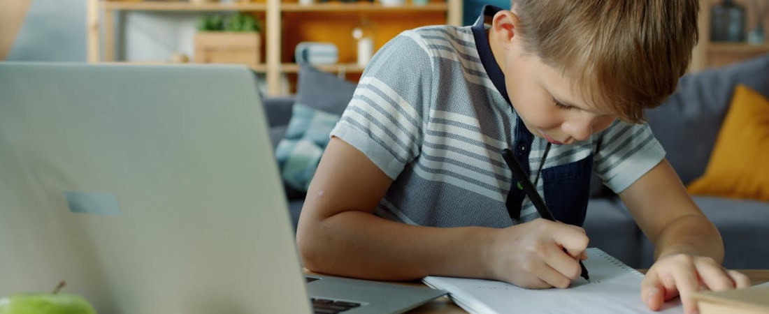 Imagem de um menino desenhando em um caderno ao lado de um laptop, exemplificando como combinar inglês online e offline crianças para um aprendizado completo.