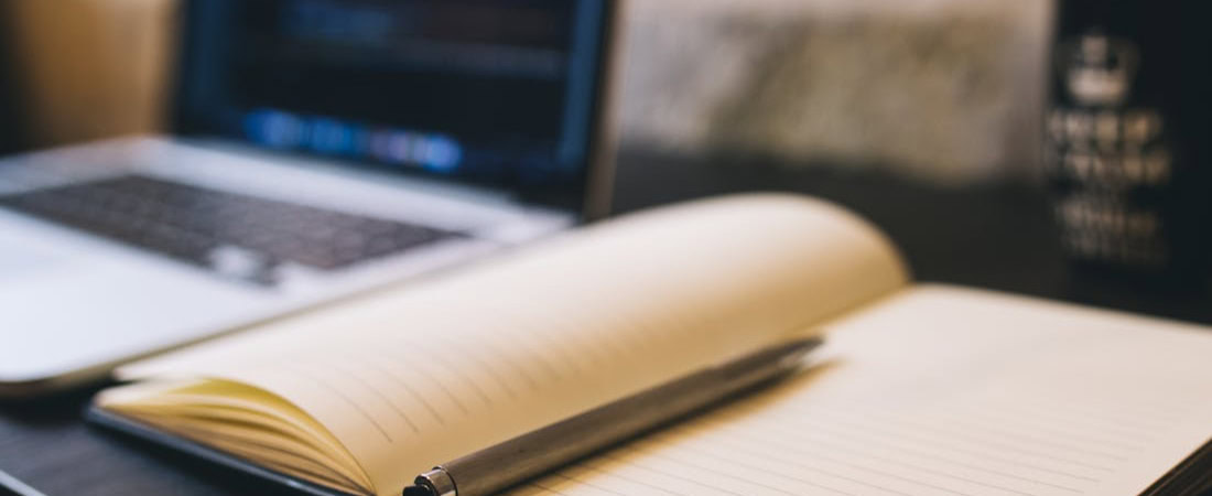 Imagem de um caderno e um notebook, representando um plano de estudo de inglês online.