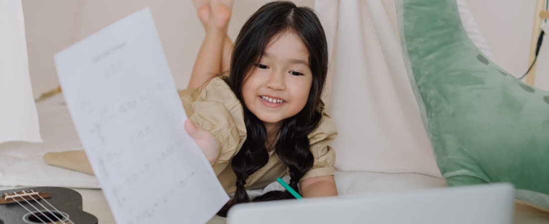 Menina sorridente em frente ao laptop mostrando seus exercícios de inglês, exemplificando o progresso e quanto custa Open English Junior em valor acadêmico.