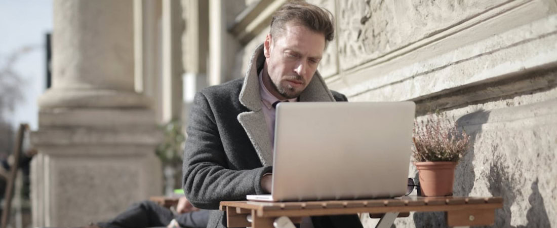 Imagem de um homem com um laptop ao ar livre, representando como falar inglês com fluência.