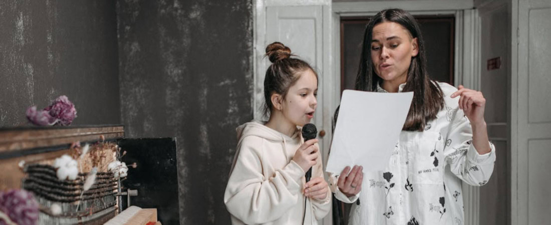 Imagem de uma menina e uma mulher cantando e lendo as notas que representam técnicas para melhorar a pronúncia do inglês em crianças.