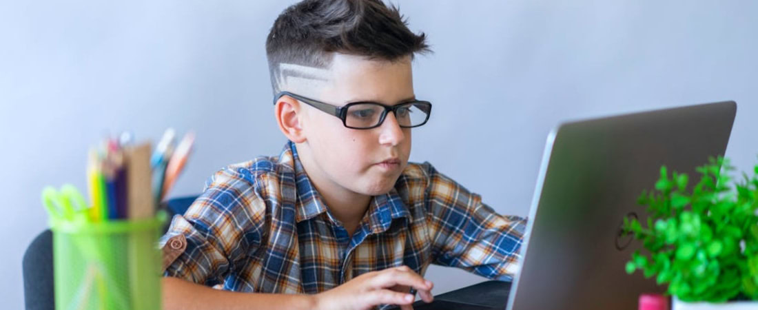 Imagem de uma criança em um ambiente colorido e estudando em frente a um laptop, fazendo referência a motivar crianças a aprender inglês online.