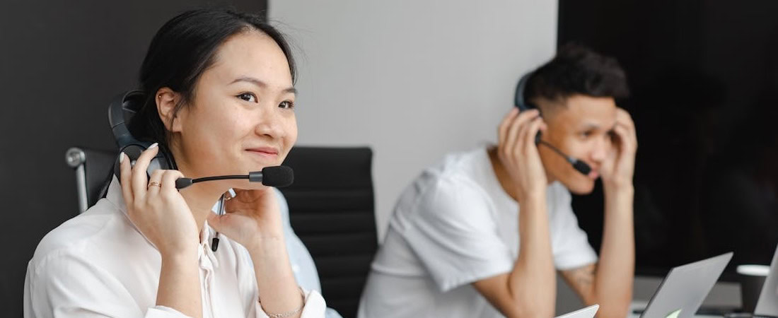 Imagem de dois jovens profissionais trabalhando em um escritório dinâmico, ambos sorridentes enquanto usam headsets com microfone, representando o ambiente ideal para quem busca ganhar fluência em inglês trabalhando.
