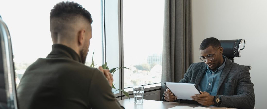 Imagem de um recrutador ou executivo de óculos analisando atentamente uma pasta de documentos durante uma reunião com um candidato, um cenário típico que exige dominar o inglês para entrevistas de emprego.