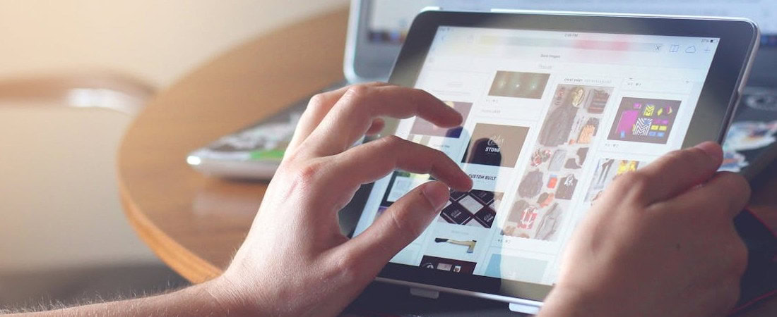 Imagem de mãos interagindo com a tela de um tablet que mostra diferentes opções de cursos, enquanto o usuário navega na internet para escolher o melhor plano anual inglês online.